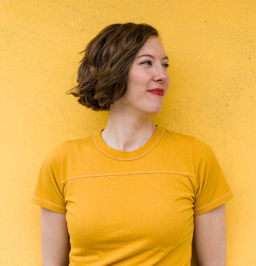 A white woman with short brown hair in a yellow shirt looks to the right.